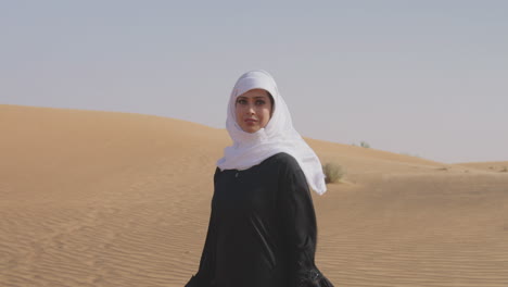 Porträt-Einer-Schönen-Muslimischen-Frau-In-Weißem-Hijab-Und-Traditionellem-Schwarzem-Kleid,-Die-In-Einer-Windigen-Wüste-Posiert