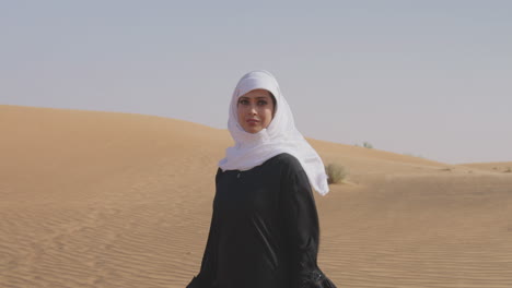 retrato de una hermosa mujer musulmana con hiyab blanco y vestido negro tradicional posando en un desierto ventoso