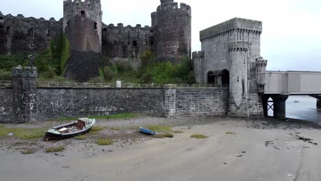 Historic-Conwy-castle-aerial-view-of-Landmark-town-ruin-stone-wall-battlements-tourist-attraction-low-orbit-across-moored-boats