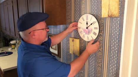 man adjusting clock for time on kitchen wall