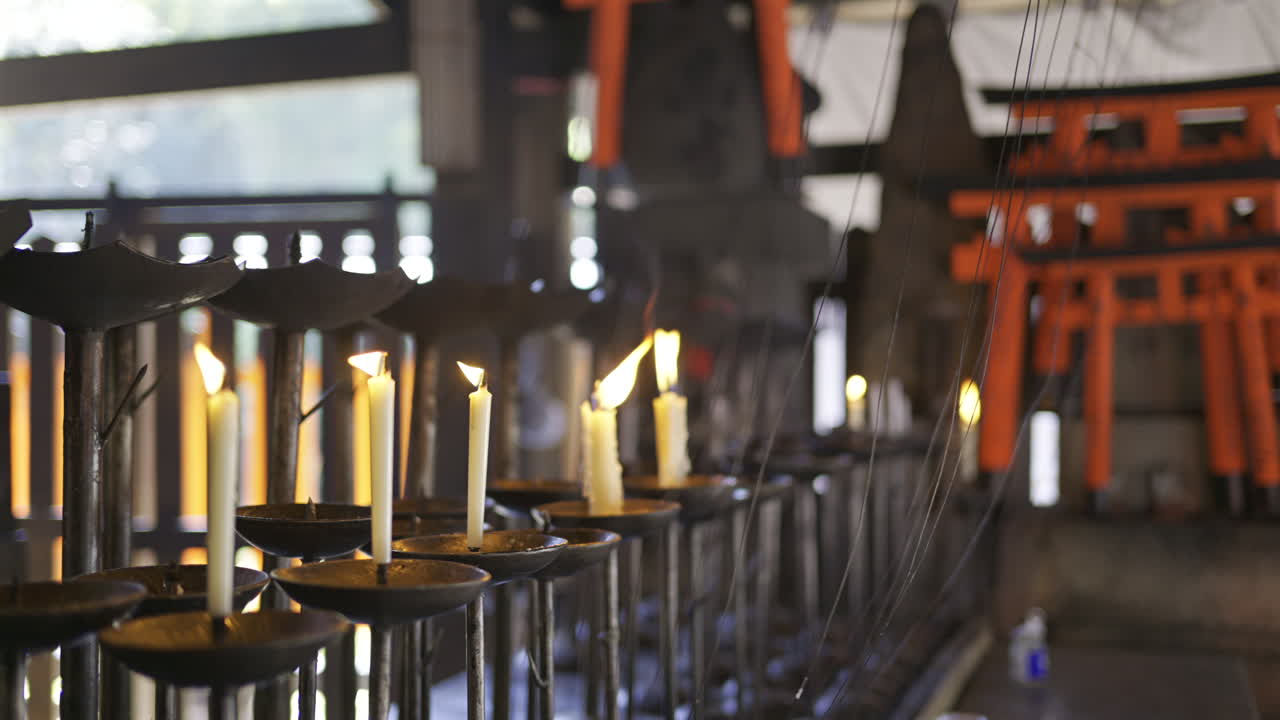 Candle lighting ritual taking place in a historic shrine. Candles illuminate the space, casting a warm glow amidst traditional architecture and vibrant colors. Kyoto, Japan, Fushimi Inari
