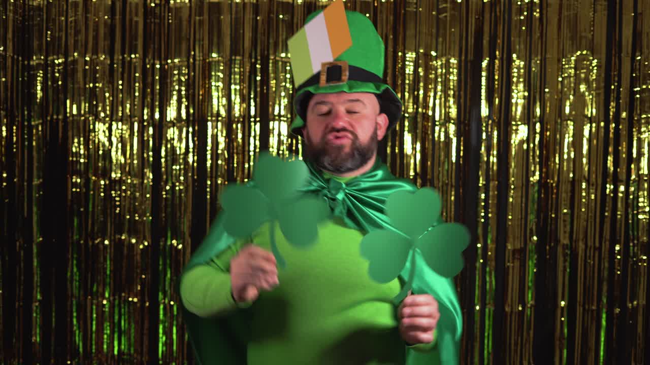 un leprechaun anciano celebra el día de san patricio sosteniendo dos hojas de trébol y bailando con ellas.