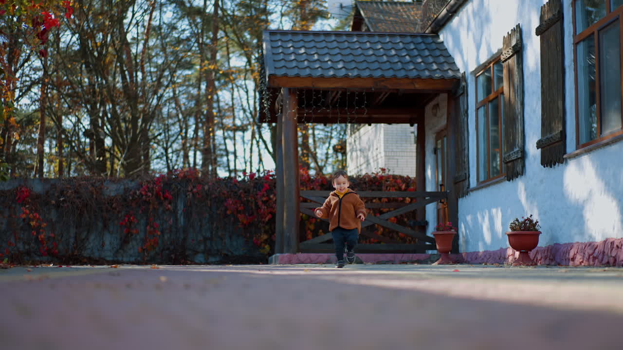 Joyful Caucasian toddler running by the yard in autumn. Energetic and active walk outdoors on sunny day.