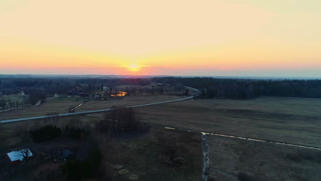 Aerial-drone-shot-over-water-canal-surrounded-by-rural-landscape-beside-road-network-during-sunrise