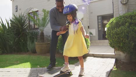 Feliz-Padre-Afroamericano-Enseñando-A-Su-Hija-A-Patinar-Frente-A-La-Casa