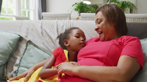 feliz abuela afroamericana y nieta abrazándose y hablando en el sofá