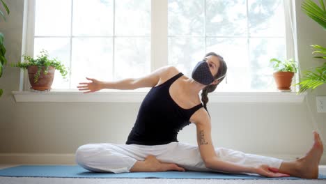 beautiful young woman does yoga stretches in her home while wearing a medical mask