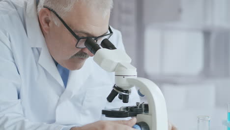 bearded caucasian male researcher wearing protective glasses and working with a microscope spbas. scientist using microscope in a laboratory. search for coronavirus vaccine. high quality 4k footage