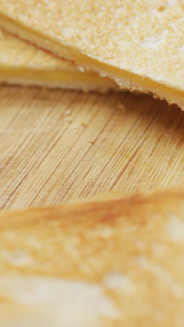 Video of slices of toasted cheese white bread sandwiches on wooden chopping board background