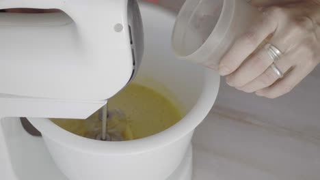 Closeup-of-a-woman's-hand-pouring-oil-onto-a-batter-being-mixed