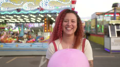 mujer feliz con cabello rojo sonríe a la cámara con algodón de azúcar y fondo claro