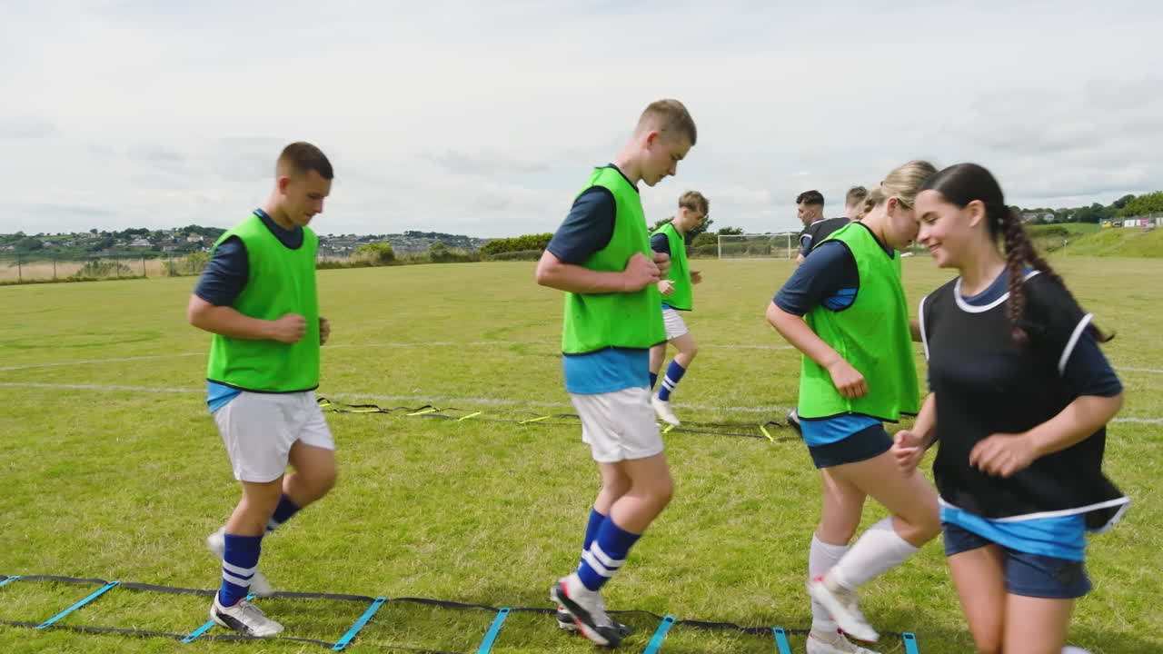 Male and female soccer players warming up and avoiding obstacles with coach on pitch