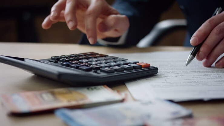 Primo piano di mani di uomo che premono i pulsanti della calcolatrice, contando tasse e fatture finanziarie.