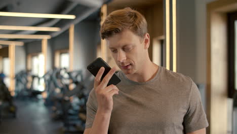 Confident-sportsman-talking-on-phone-at-gym.-Fitness-man-standing-in-sport-club.