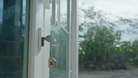 the house key for unlocking a new house is plugged into the door. the keychain is blowing in the wind.