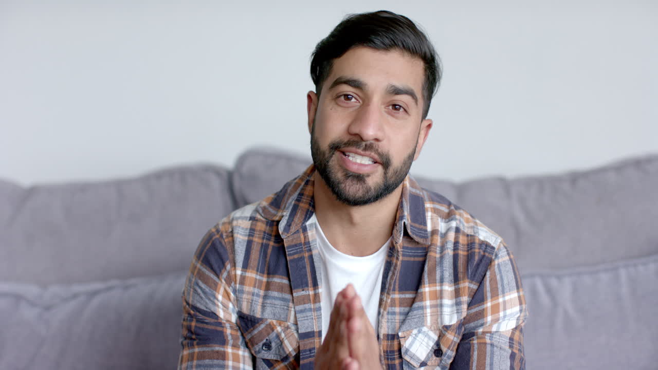 Young Asian man seated on a couch at home, on video call