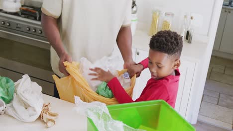 happy african american father and son sorting waste in kitchen, in slow motion
