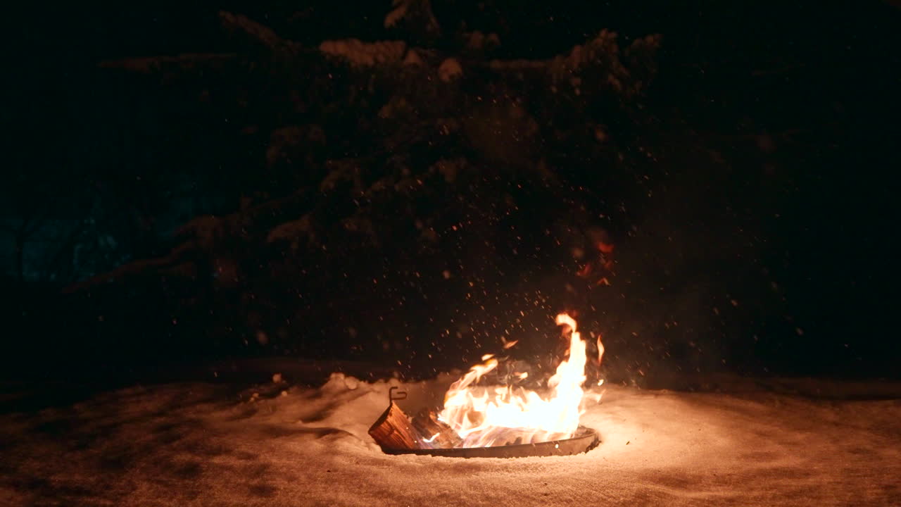 la nieve cae en invierno mientras las llamas del fuego de leña caliente iluminan la oscuridad.