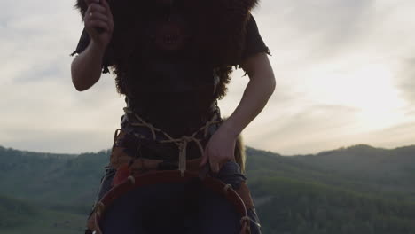 Drummer-taps-tambourine-against-distant-mountains-at-sunset