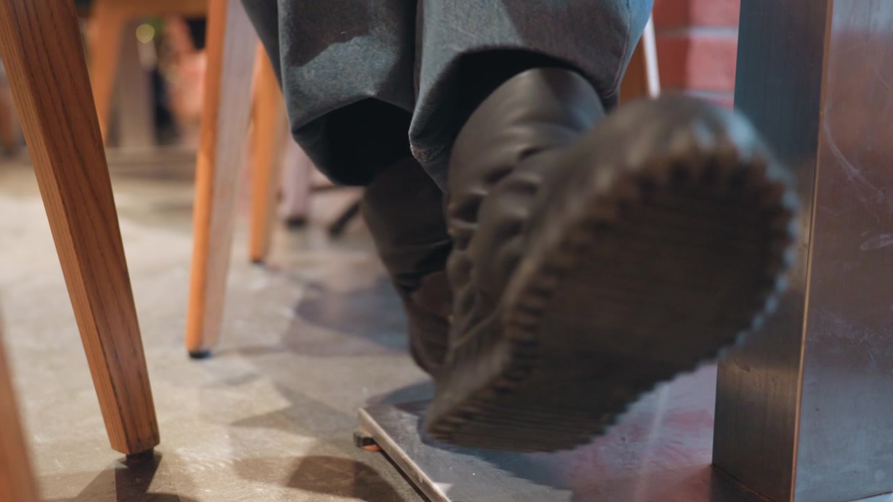 Gros plan sur les pieds d'une personne en bottes, tapant et se croisant sous une table.