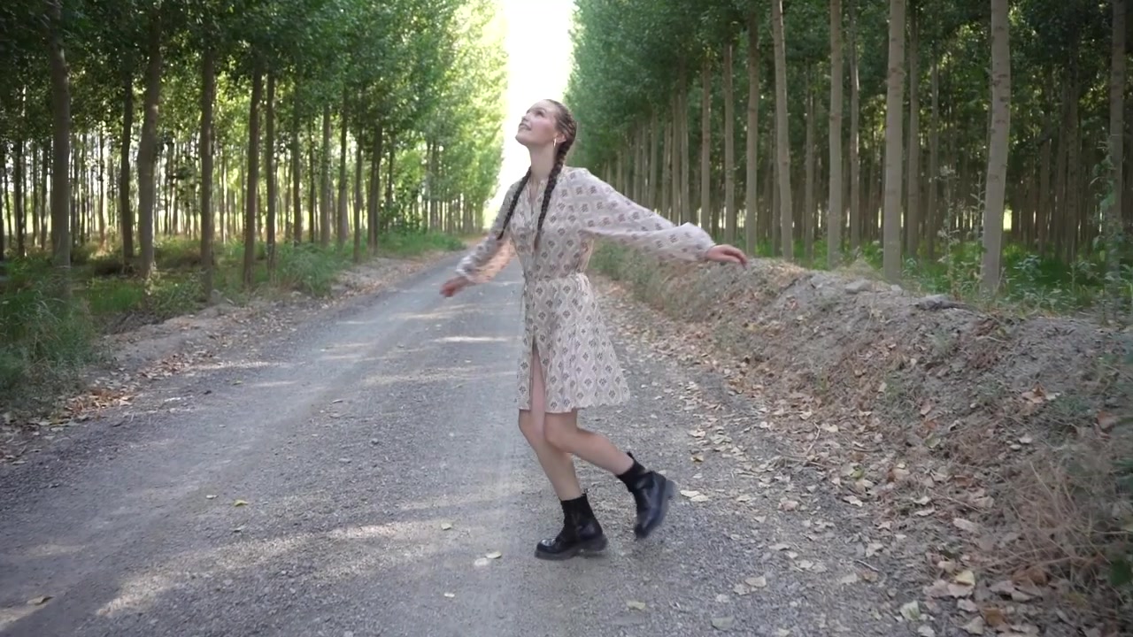 Una graziosa ragazza balla felicemente su un pittoresco sentiero di ghiaia, circondata da alberi rigogliosi.