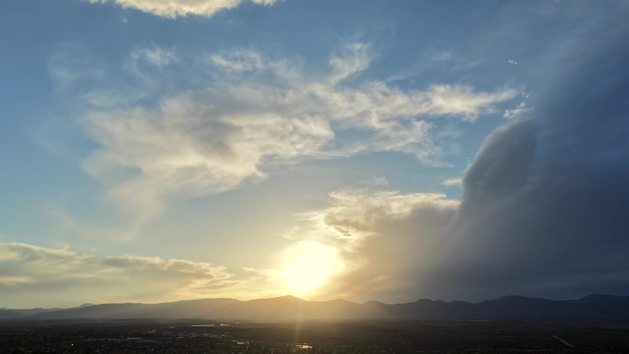 A drone timelapse capturing the sun emerging brightly from a distinct wing-shaped cloud formation. Simultaneously, a dense upper layer of atmospheric clouds moves in overhead across the sky.