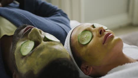 Happy-diverse-couple-lying-with-masks-and-pieces-of-cucumber-on-eyes-in-bathroom