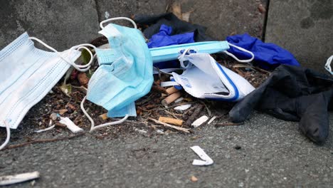 dirty disposable corona virus face masks and latex gloves among cigarette rubbish on street curb dolly right