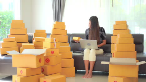 with a package that needs shipping in one and one hand on her laptop keyboard, a young attractive businesswoman scrambles to get all her shipping done