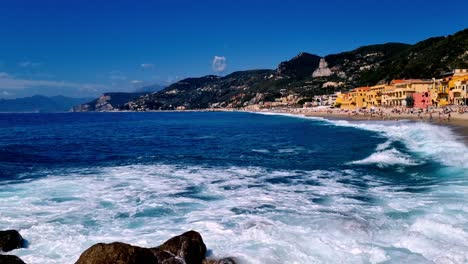 Toma-Estática-De-La-Riviera-Italiana-Con-Olas-Rompiendo-En-La-Playa-Y-Lugareños-Jugando-Y-Tomando-El-Sol