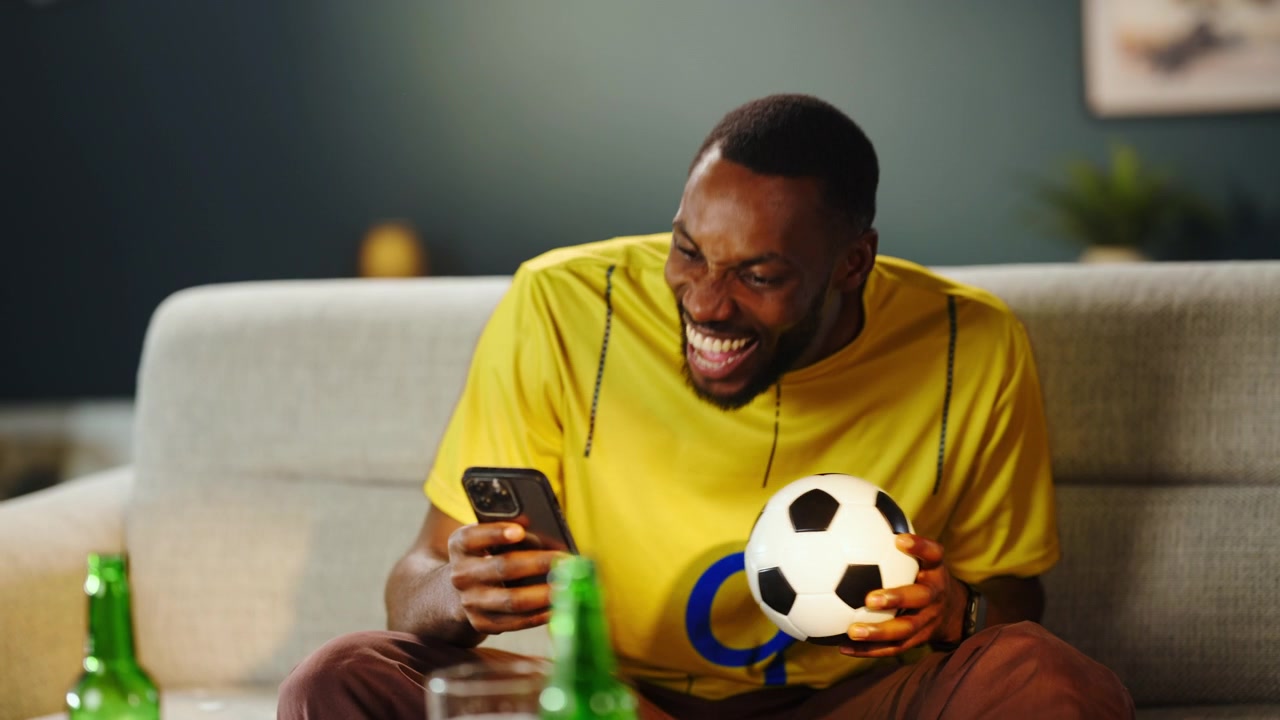 Tifoso di calcio entusiasta che guarda la partita sullo smartphone a casa