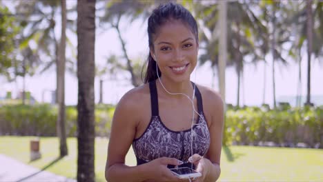 Smiling-Asian-woman-in-earphones-with-smartphone-in-hand-in-park