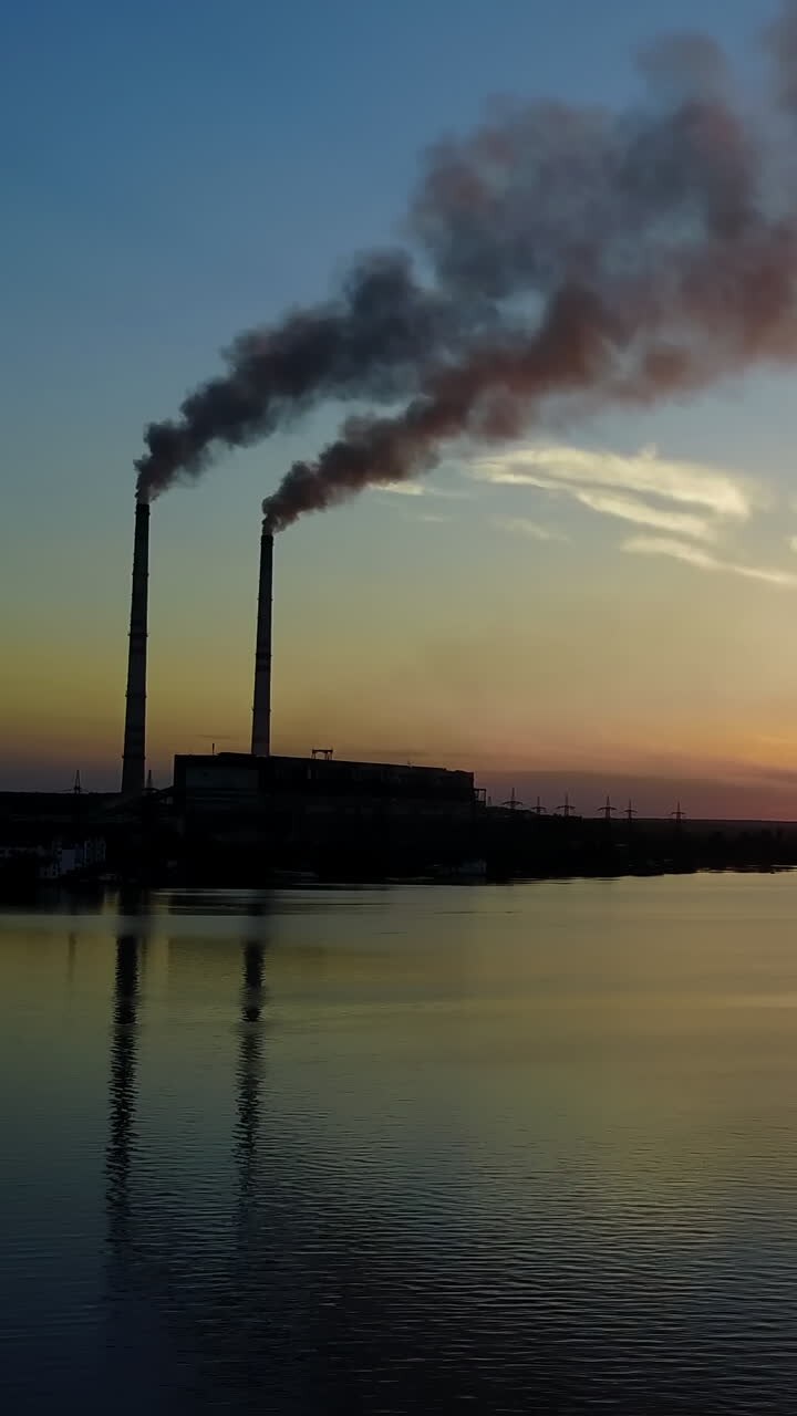 Power Station Over River. Power station with pipes of which poured smoke on a river at sunaset Vertical video