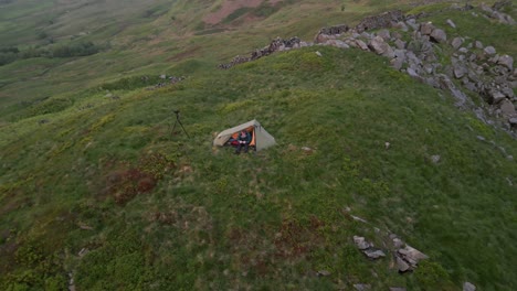 A-solo-traveller-made-his-tent-on-a-green-rocky-hill-at-sunset-towards-Errwood-Reserve,-UK