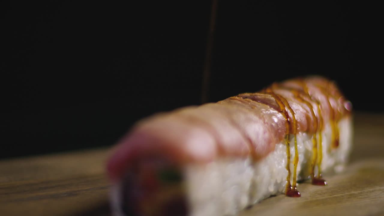 Chef pouring appetizing sushi set by sauce on wooden board