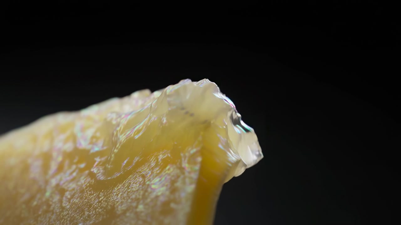 斜めからのマクロ視点、先の尖った黄琥珀色の破片。無傷の先端から、欠け、ひび割れ、引き裂かれた半透明の層へと目に見えて変化している様子を、方向性のあるリムライトの下で捉えたマクロクローズアップ。