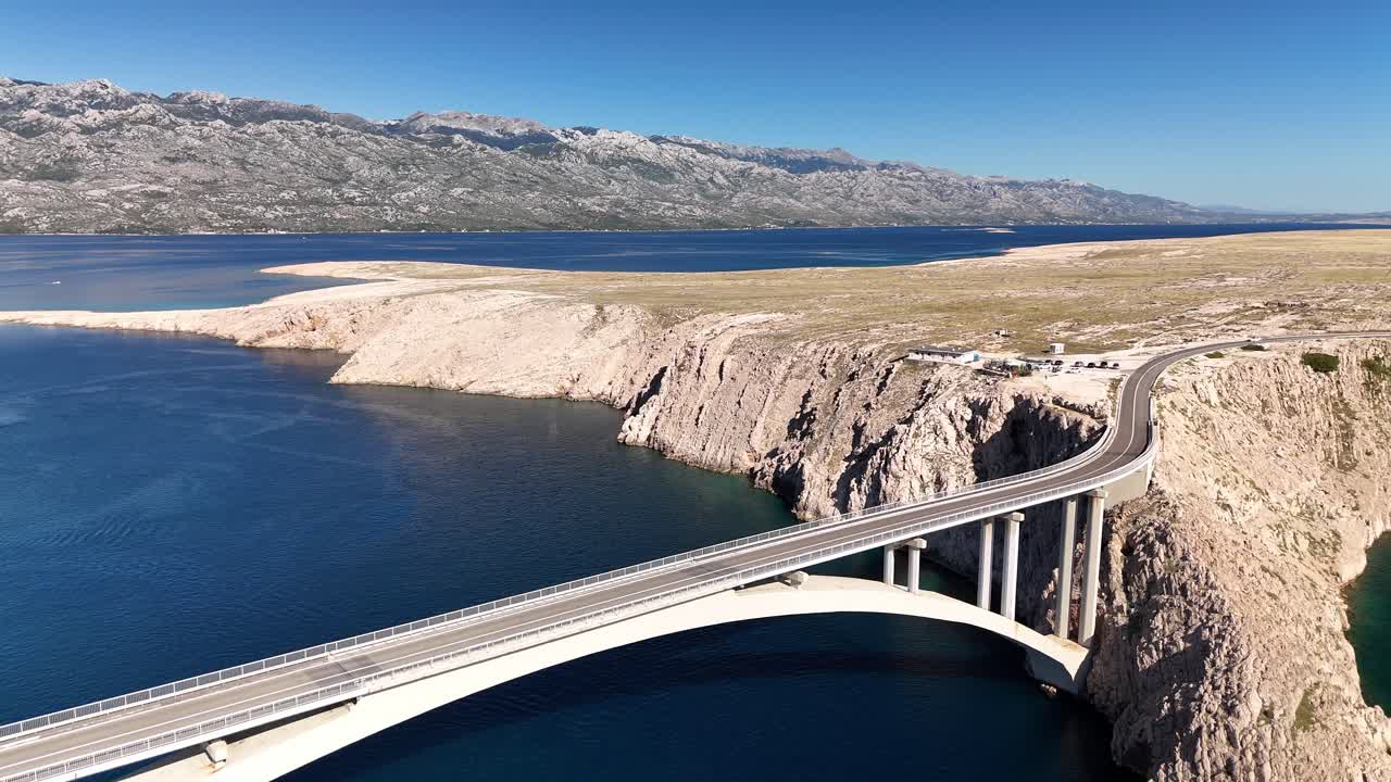Drone aerial turning over Pag Island, Croatia. Rugged rocky coastline and barren landscape with Adriatic Sea, Velebit mountains, and road crossing the Pag Bridge in summer