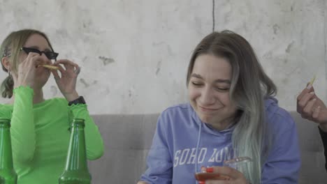 amigas felices comiendo papas fritas y divirtiéndose mientras se sientan en el sofá en casa