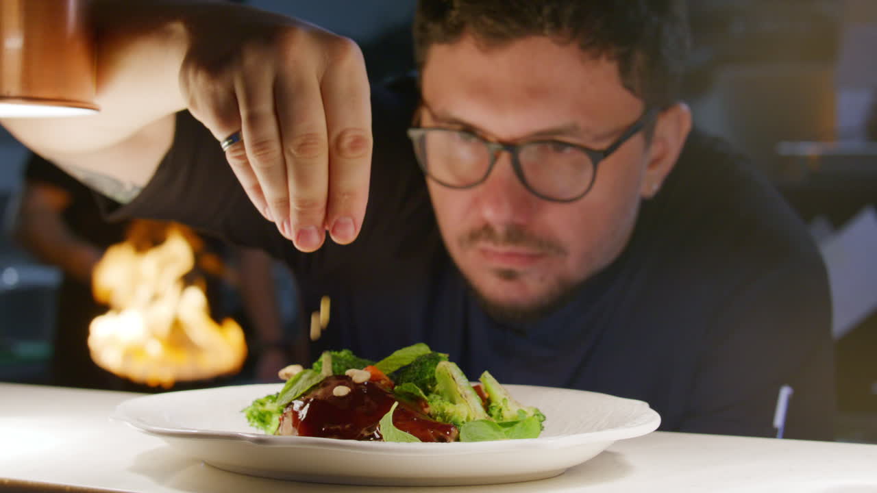 Chef spolvera pinoli su un piatto gourmet di anatra e verdure.