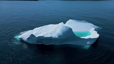 aerial footage of a large iceberg off flatrock, newfoundland, featuring vivid turquoise meltwater in calm atlantic waters.