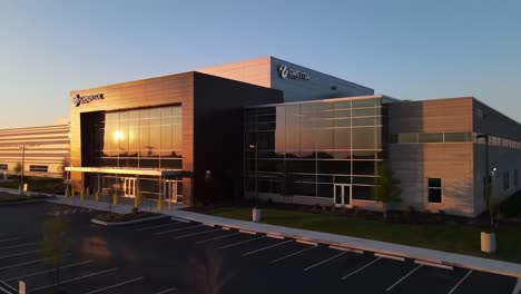 dawn breaks over a contemporary structure as the sun casts warm light on a vacant parking area. the serene atmosphere highlights the peaceful start to the day in this location.