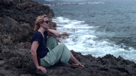 woman sitting on a cliff and watching the surf of the waves breaking on the rock