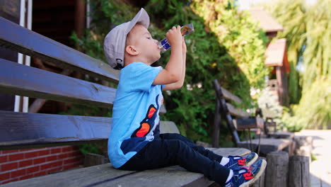 toddler boy sitting on the bench outdoors and drinks from a doy pack. kid finishes a pack and gives it to his mom.