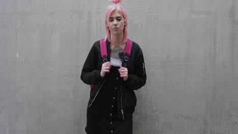 retrato de una joven chica punk estudiante de cabello rosa que busca confianza independiente mujer caucásica estilo de moda alternativa en fondo de pared de hormigón