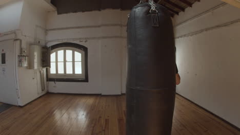 long shot of concentrated woman punching heavy bag in empty gym