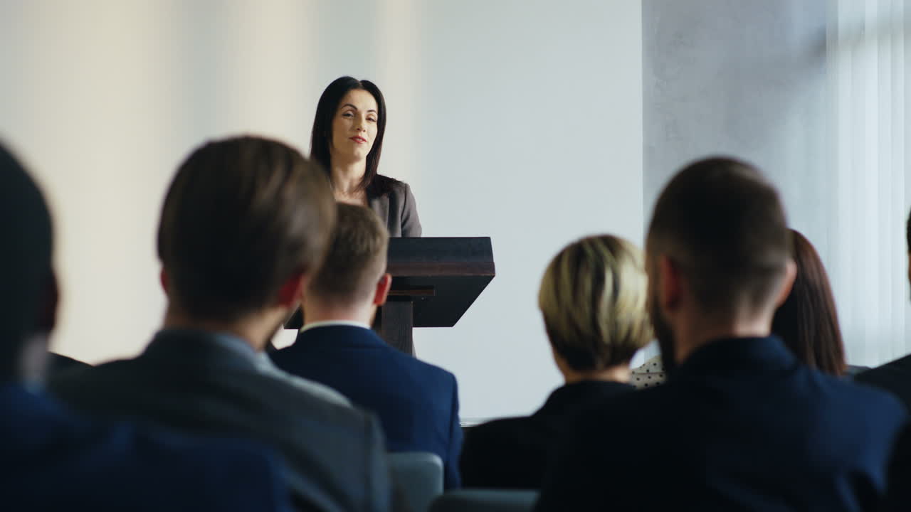 morena caucasiana jovem empresária falando em um pódio em uma grande conferência na frente de muitas pessoas