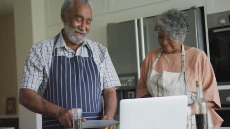 Feliz-Pareja-De-Ancianos-Afroamericanos-Cocinando-Juntos,-Usando-Una-Computadora-Portátil