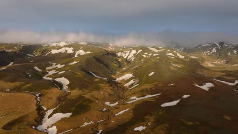 aerial landscape view of a river flowing through a mountain valley, covered in melting snow, in iceland