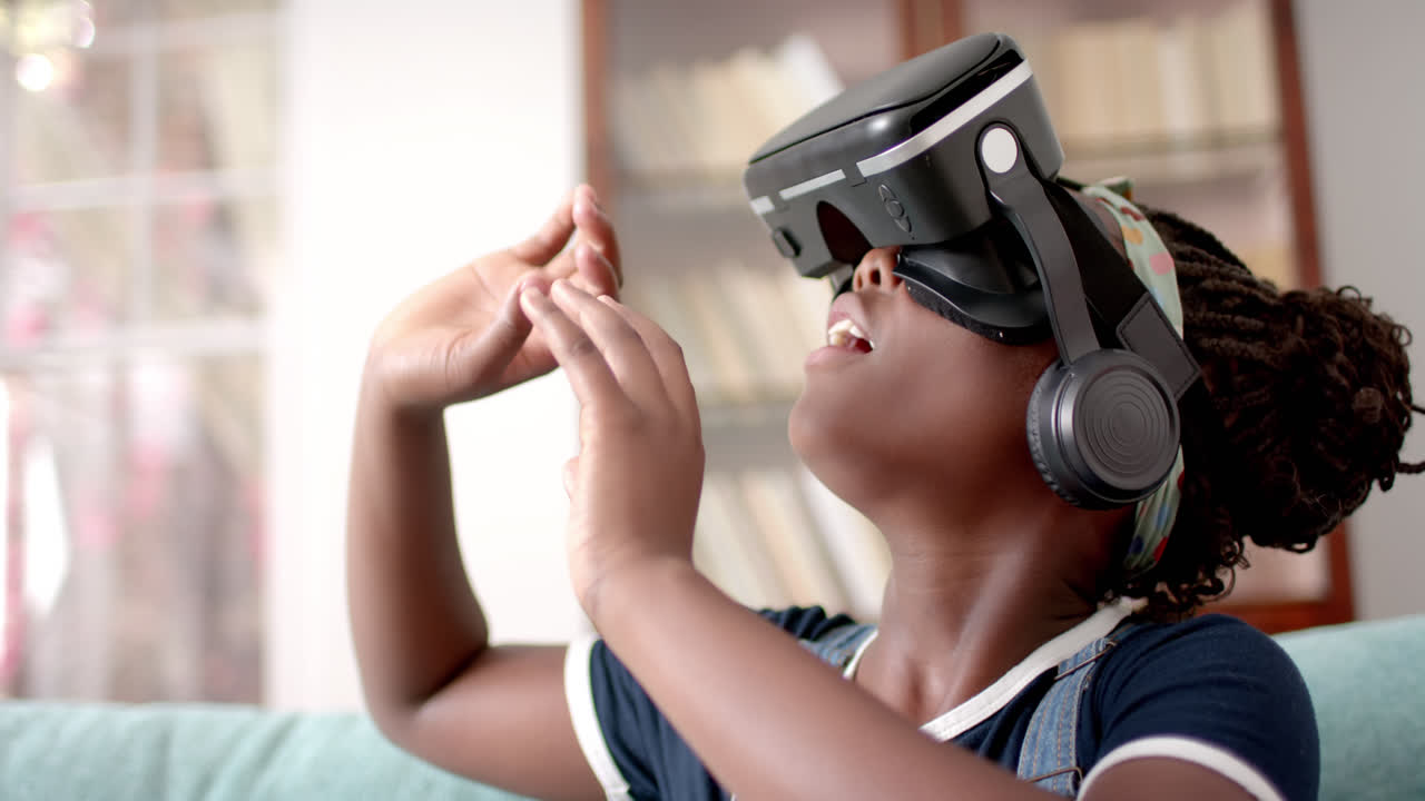 Afroamerikansk pige bruger VR-headset og rører ved virtuel skærm i stuen, slowmotion.