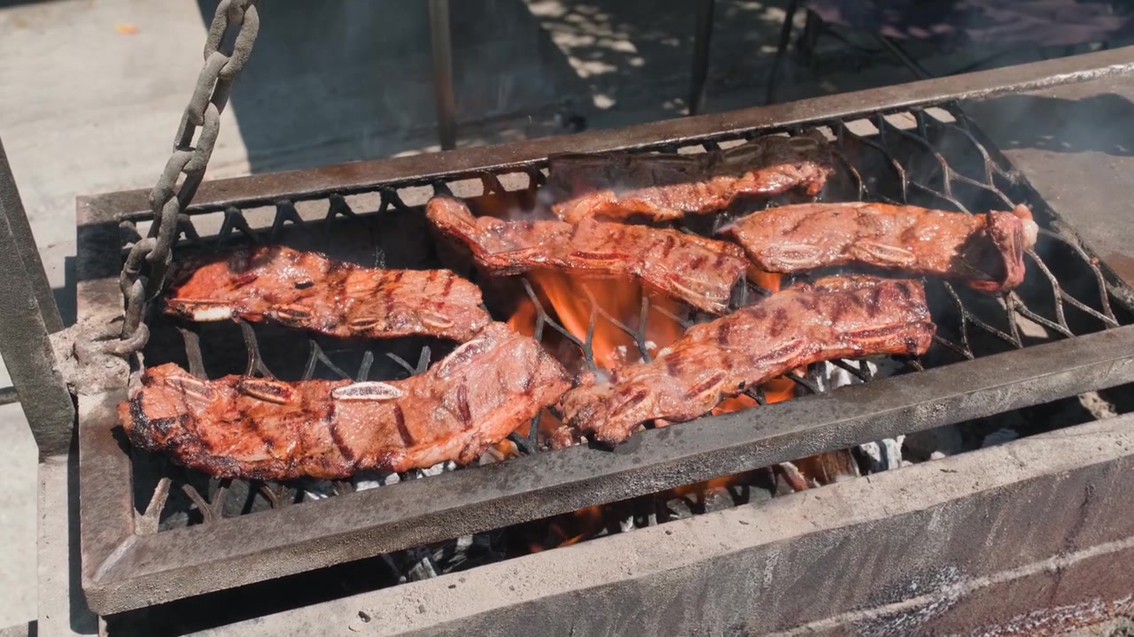 Costine di manzo condite cuociono su una fiamma viva e braci ardenti su una griglia rustica all'aperto durante la preparazione del barbecue.